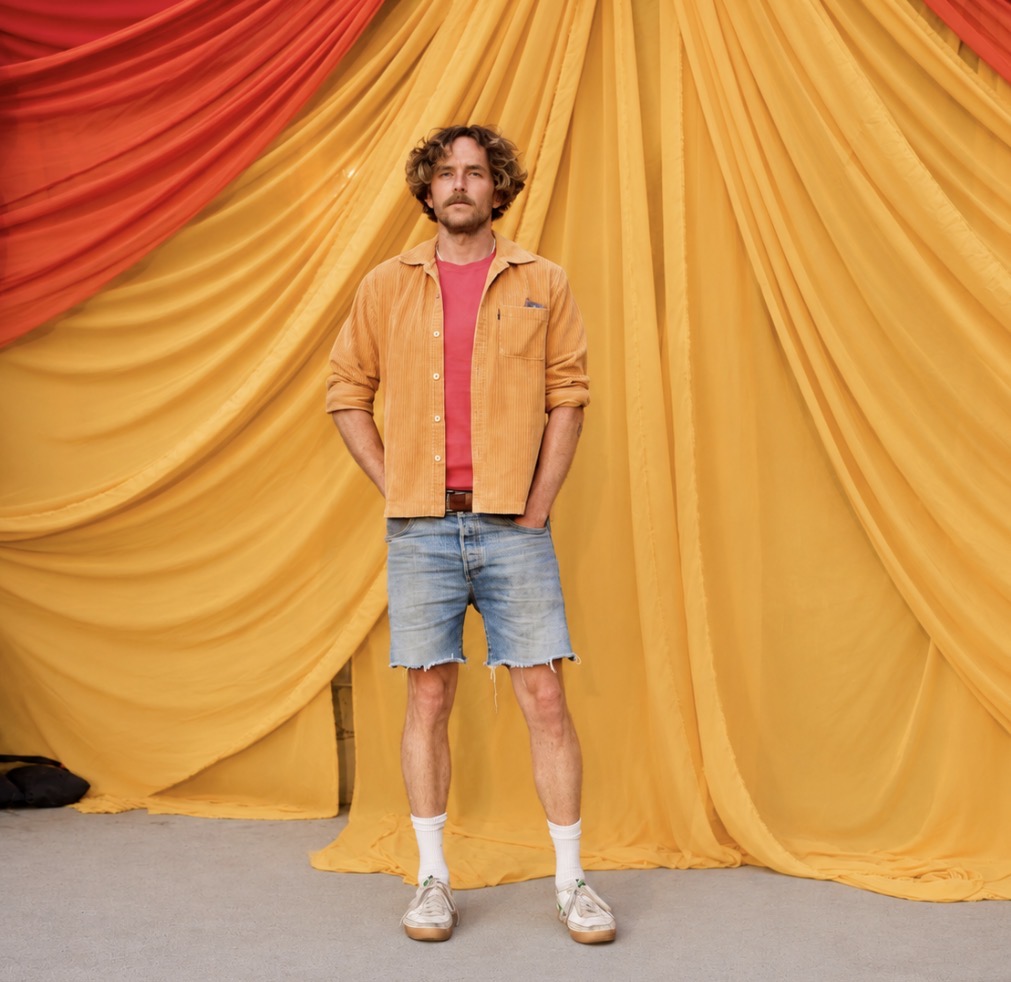 Matthew Warren standing in front of yellow and red draped fabric